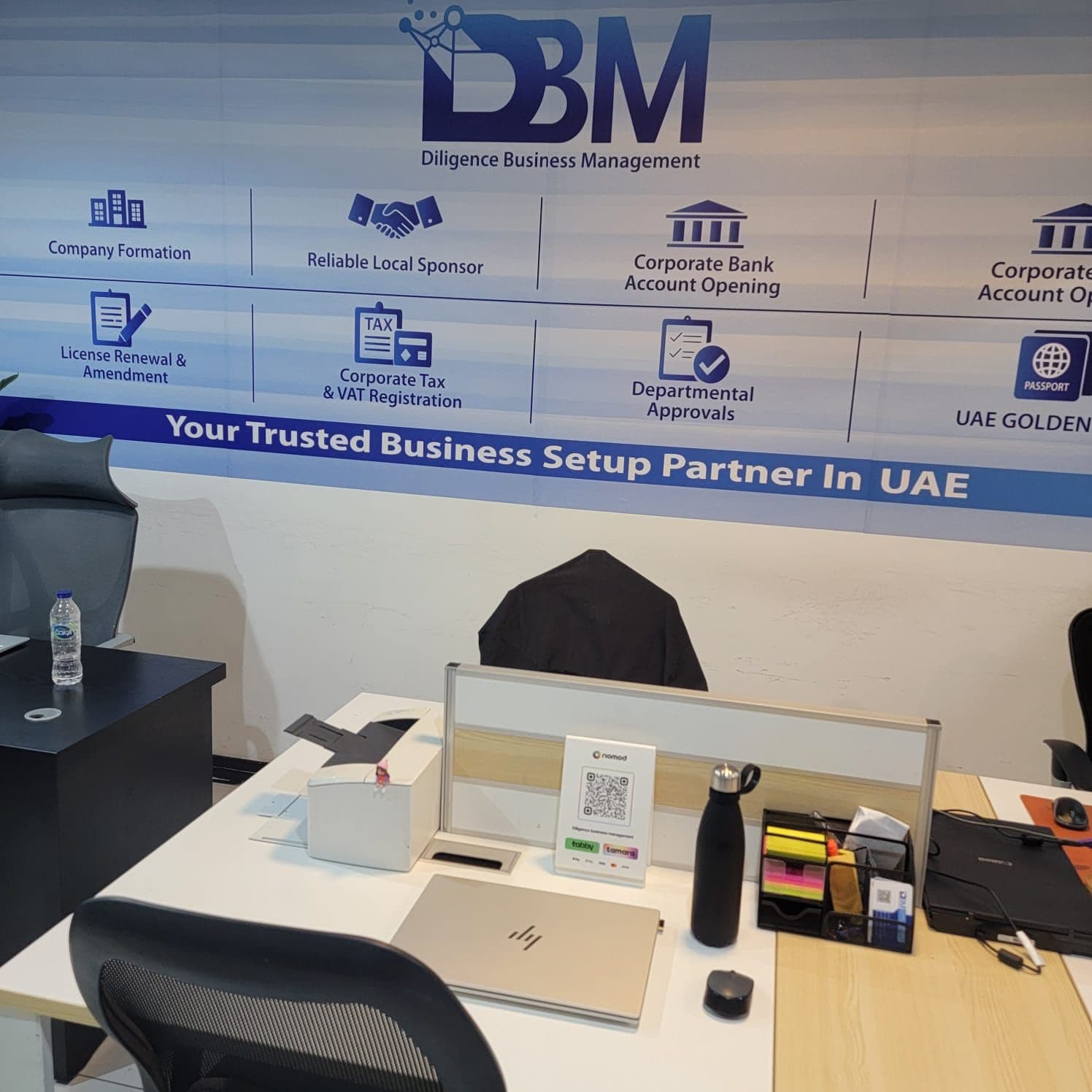 Workstation at DBM with the 'Your Trusted Business Setup Partner In UAE' branded wall